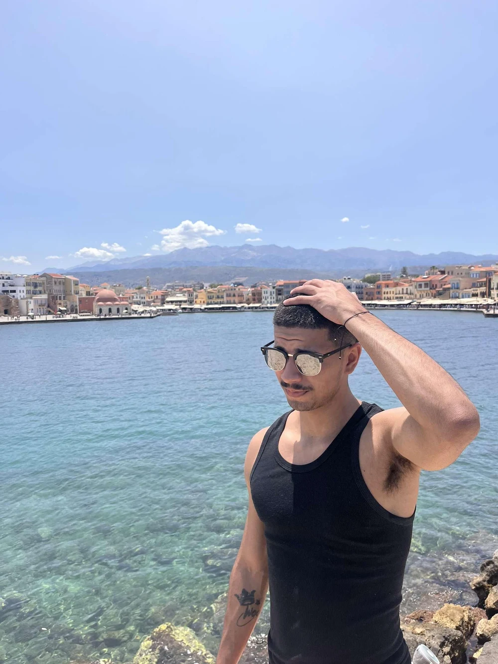 Jonathon wearing sunglasses beside the sea, with a waterfront town in the background.
